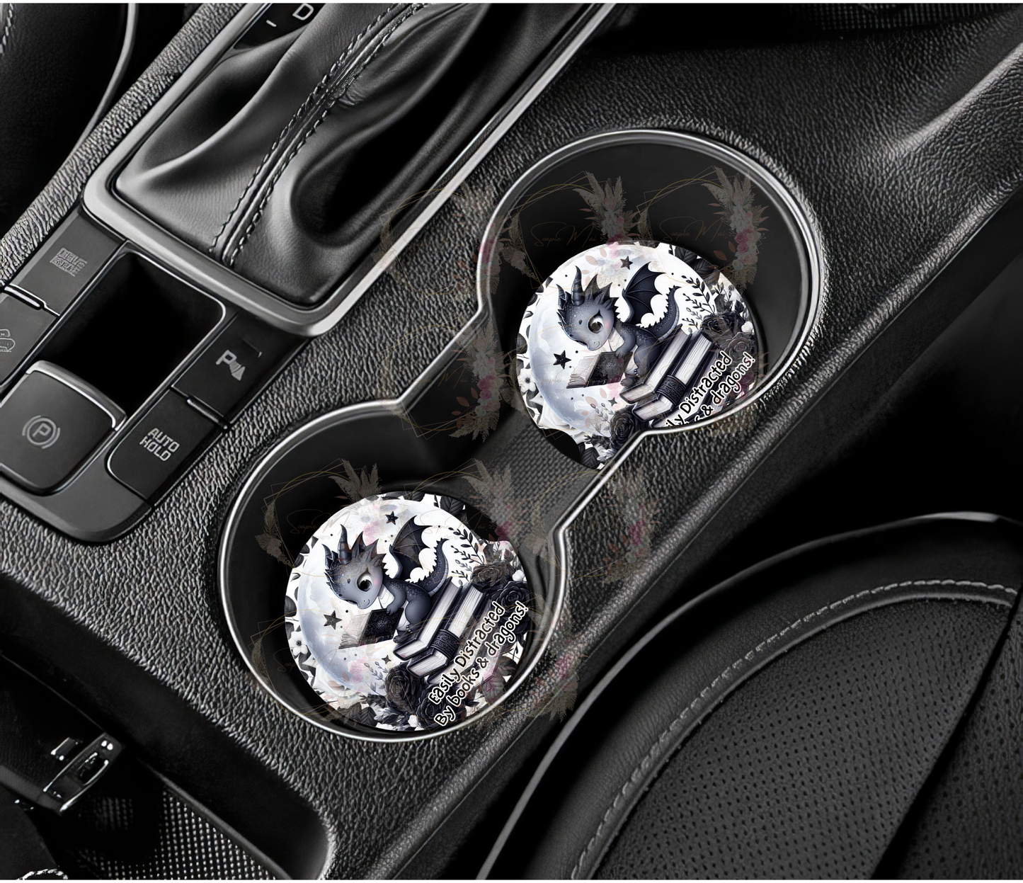 Pair of absorbent car coasters with an 'Easily Distracted by Books & Dragons' black and white design, featuring a dragon reading on books, a floral background, and a moon, protecting your vehicle's cup holders.