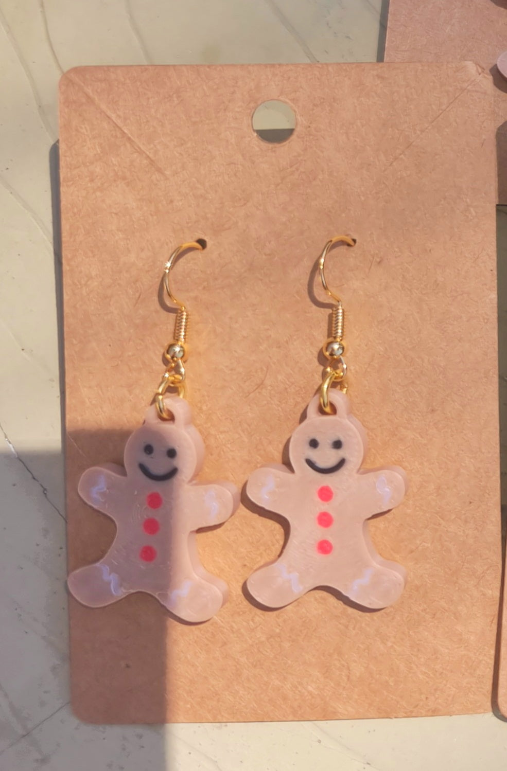 Close-up of a single handmade 3D printed gingerbread man earring, showing its charming button and smile details